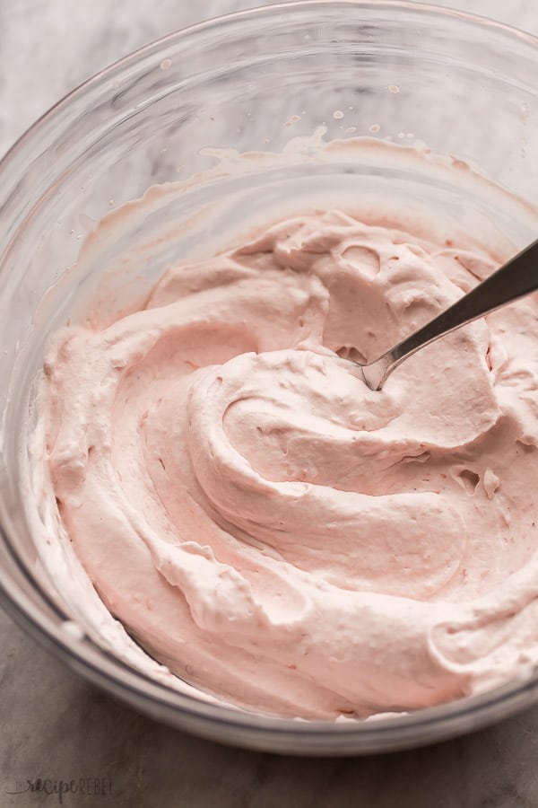 strawberry whipped cream with a metal spoon in large glass bowl on marble background