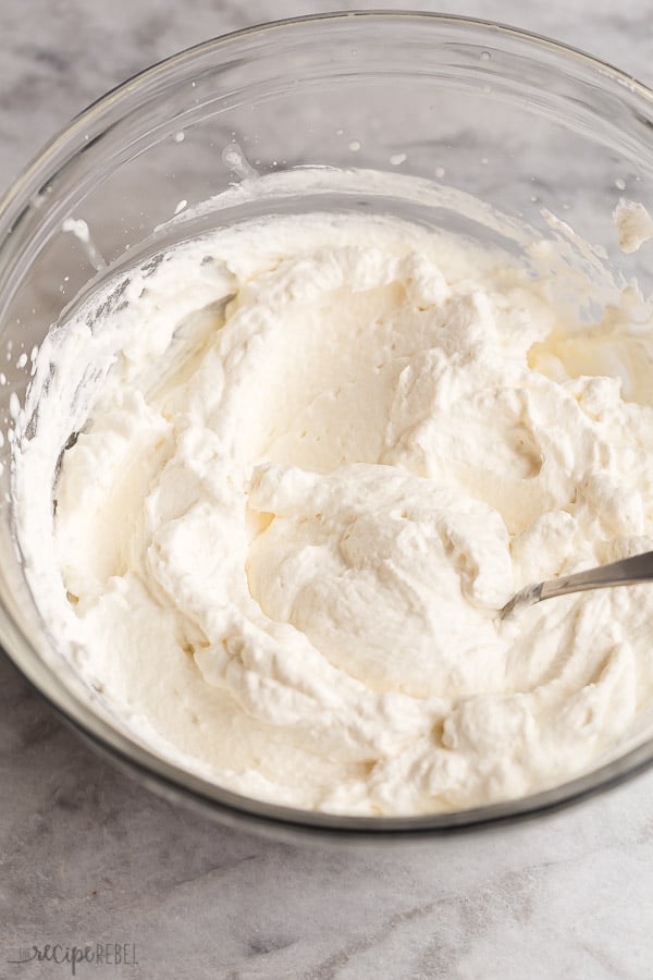 homemade whipped cream in bowl with spoon on marble background
