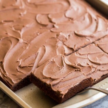 lifting a piece of chocolate sheet cake out of a sheet pan.