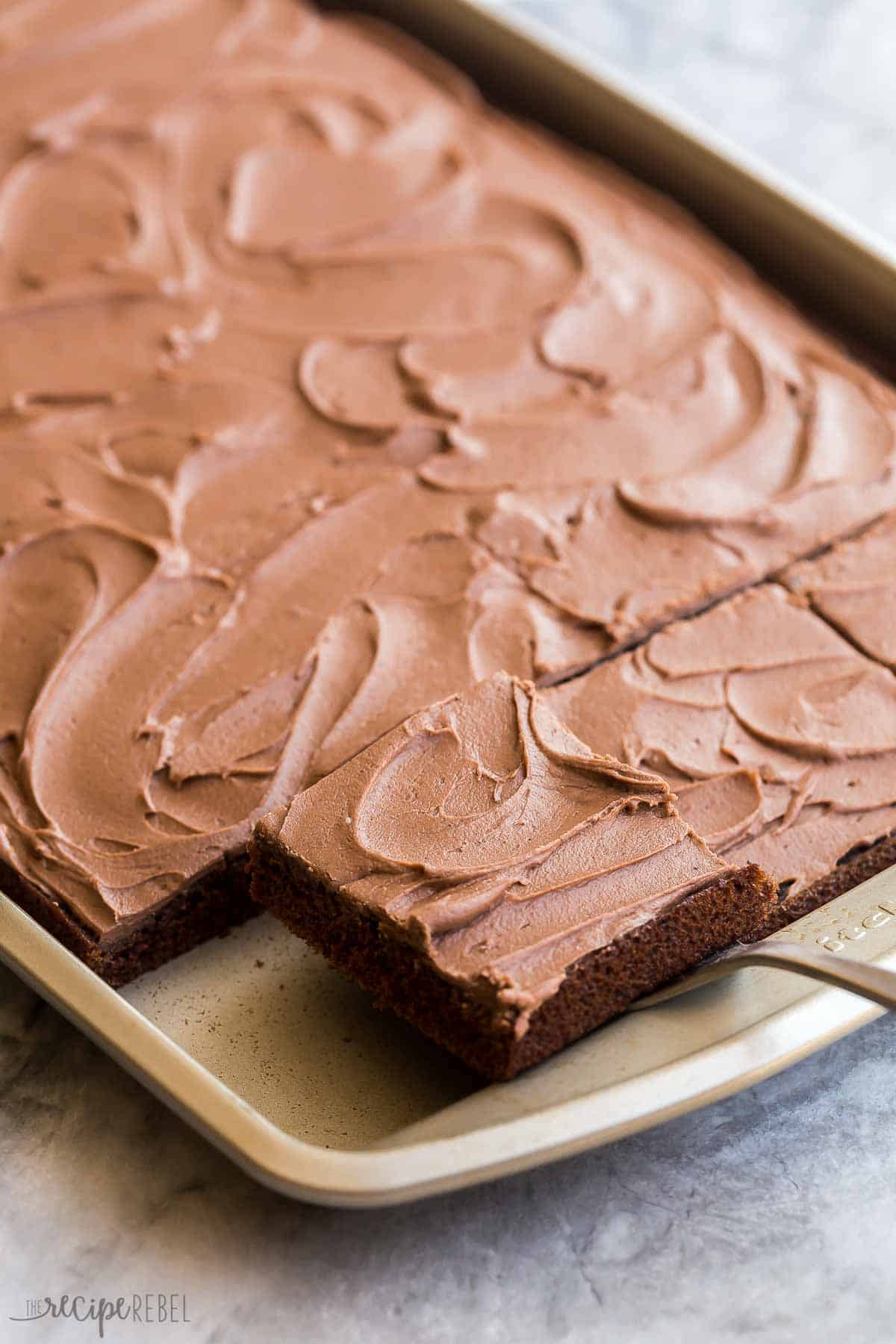 This Chocolate Sheet Cake is rich and chocolatey and so easy to make! Topped with a simple frosting made of melted butter, cocoa and sugar. It's sure to be a hit at any potluck! #chocolate #dessert #recipe | chocolate desserts | chocolate recipes | easy cake recipe | potluck dessert | holiday dessert | easy chocolate cake | easy dessert recipes lifting a piece of chocolate sheet cake out of a sheet pan.