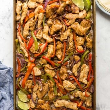 overhead image of a sheet pan with cooked chicken strips bell peppers and onions
