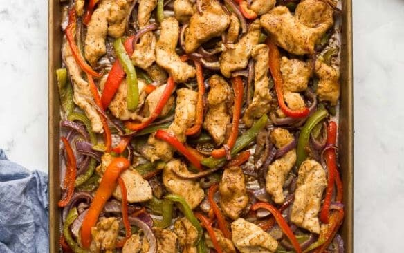 overhead image of a sheet pan with cooked chicken strips bell peppers and onions