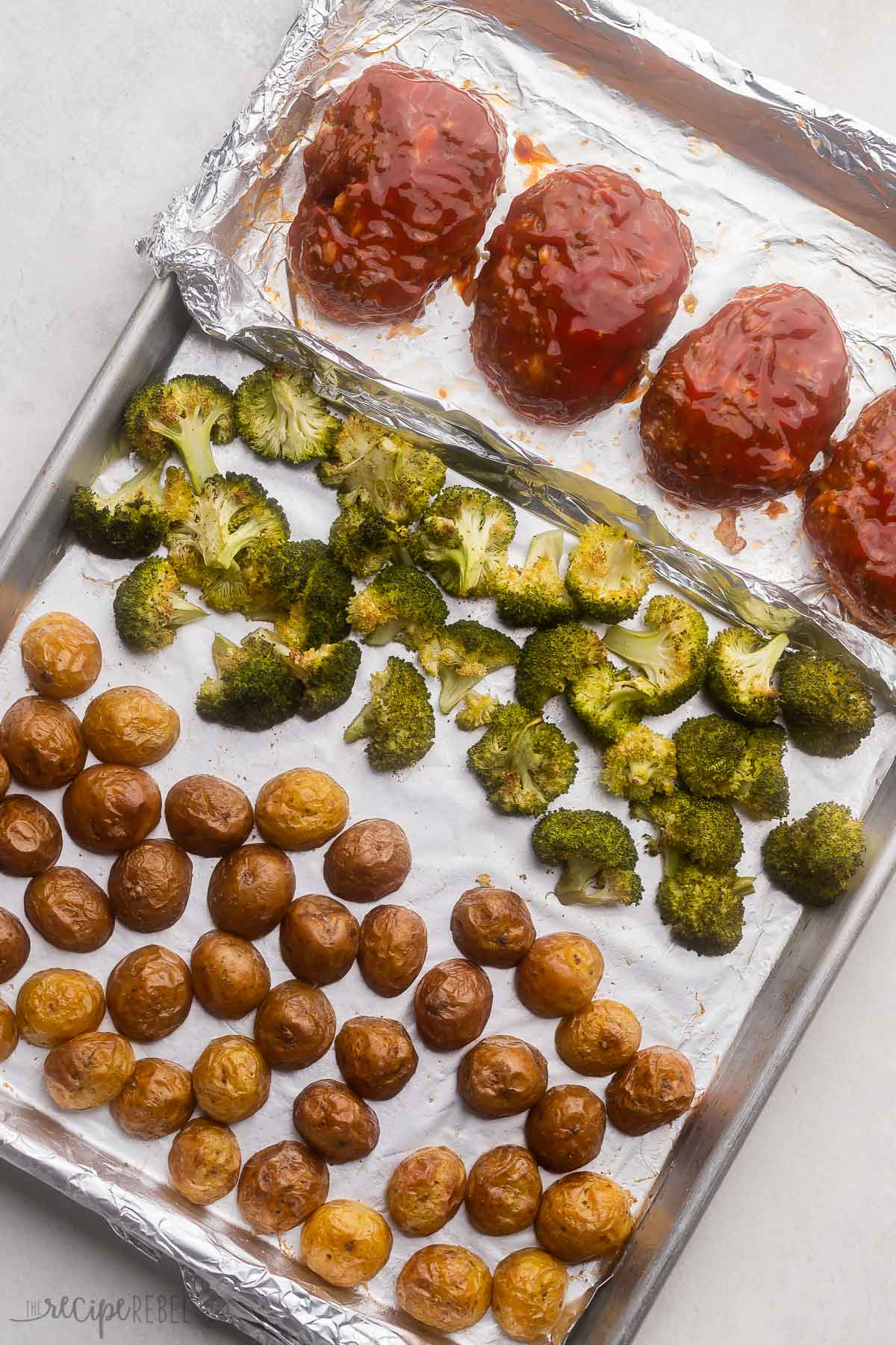 overhead image of sheet pan with mini meatloaves, roasted broccoli and potatoes.

