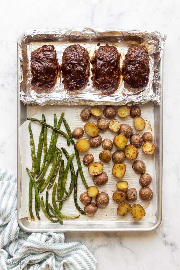 overhead image of four mini meatloaves on sheet pan with potatoes and green beans