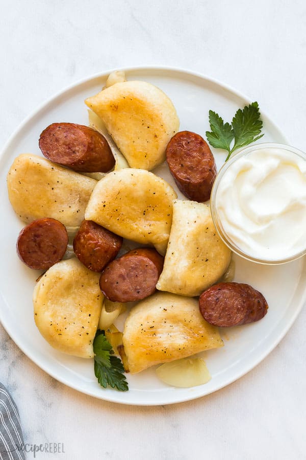 sausages and pierogis on white plate with small bowl of sour cream
