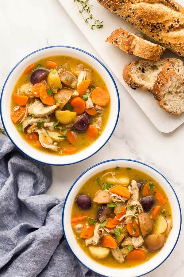 two white bowls of chicken stew with crusty bread on the side