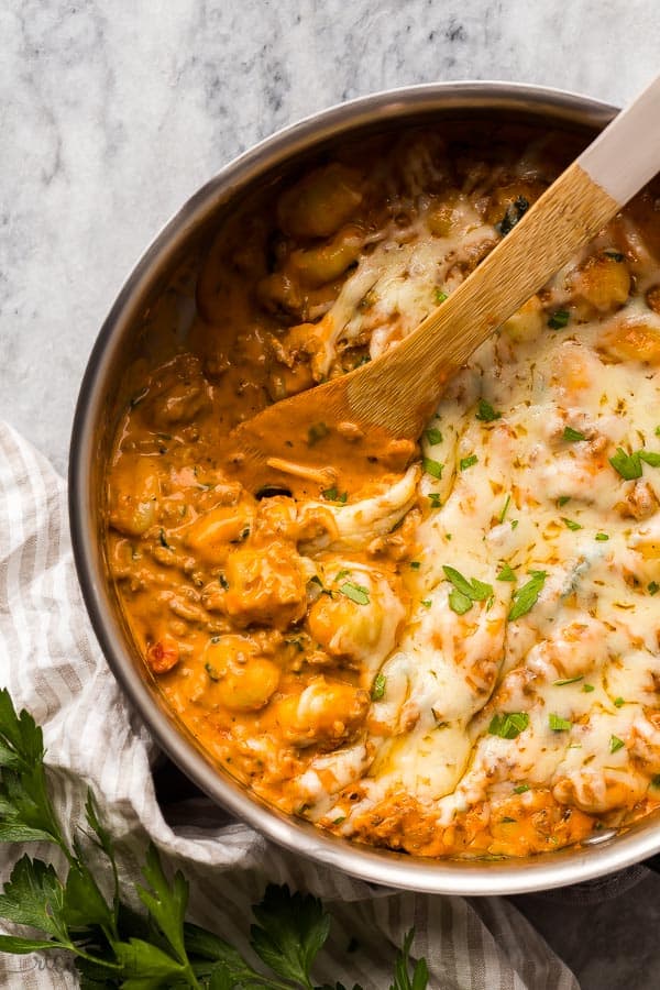 close up image of italian sausage gnocchi in skillet with wooden spoon