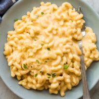 blue bowl with macaroni and cheese topped with fresh parsley and a fork