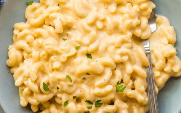 blue bowl with macaroni and cheese topped with fresh parsley and a fork