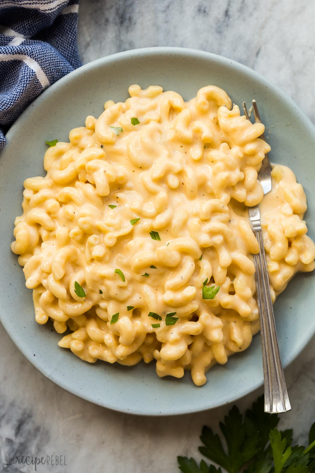 blue bowl with macaroni and cheese topped with fresh parsley and a fork