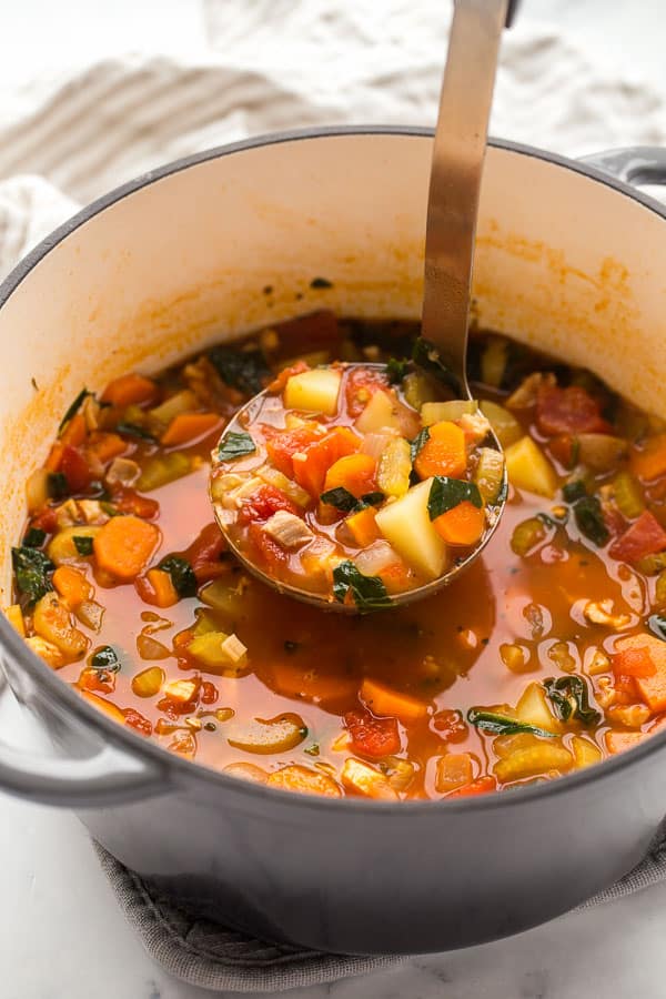 ladle scooping chicken vegetable soup from dutch oven