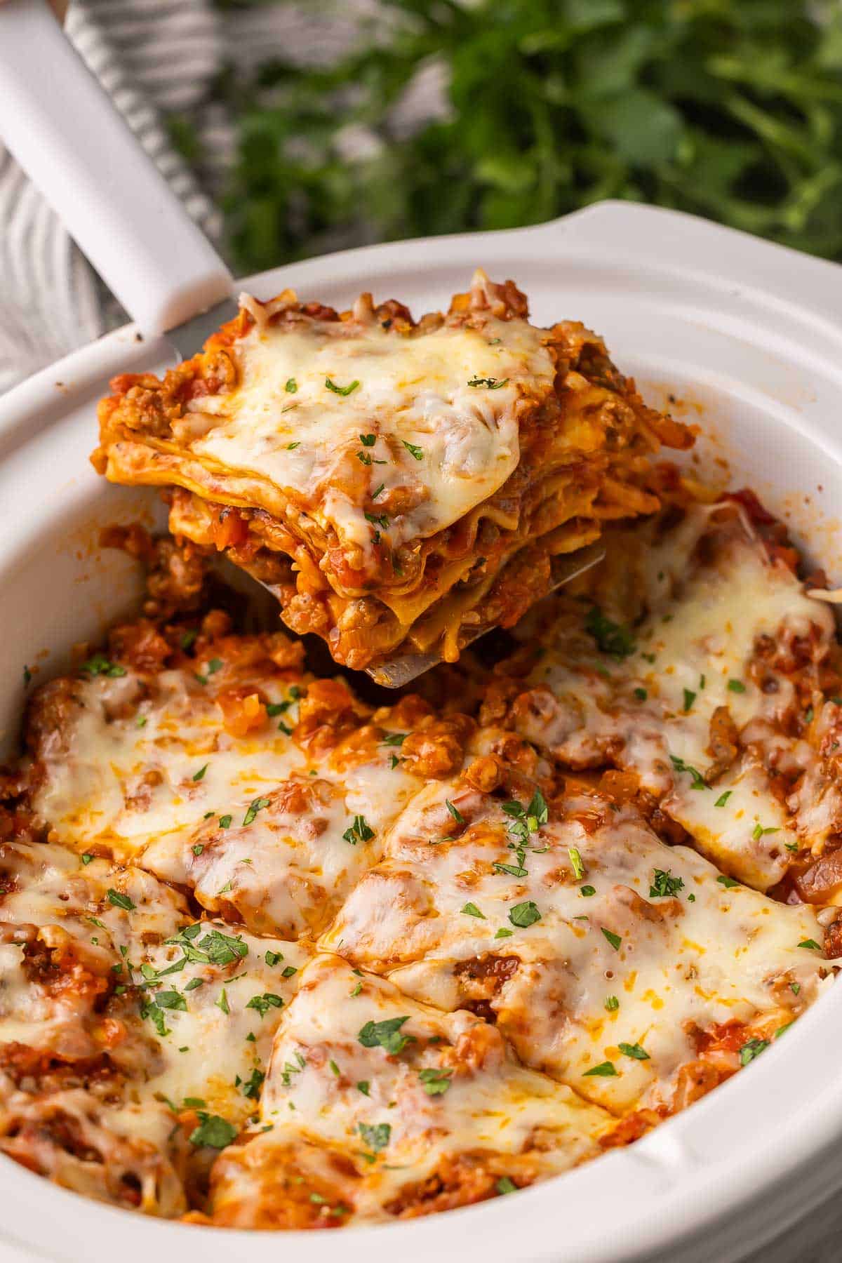 This Crockpot Lasagna is an easy set-it-and-forget-it crockpot meal made with tender noodles, savory meat sauce, and melty cheese. #crockpot #slowcooker #dinner #recipe | dinner ideas | italian sausage | ground beef recipe | comfort food | slow cooker meals | crockpot lasagna being pulled out of slow cooker with a spatula.