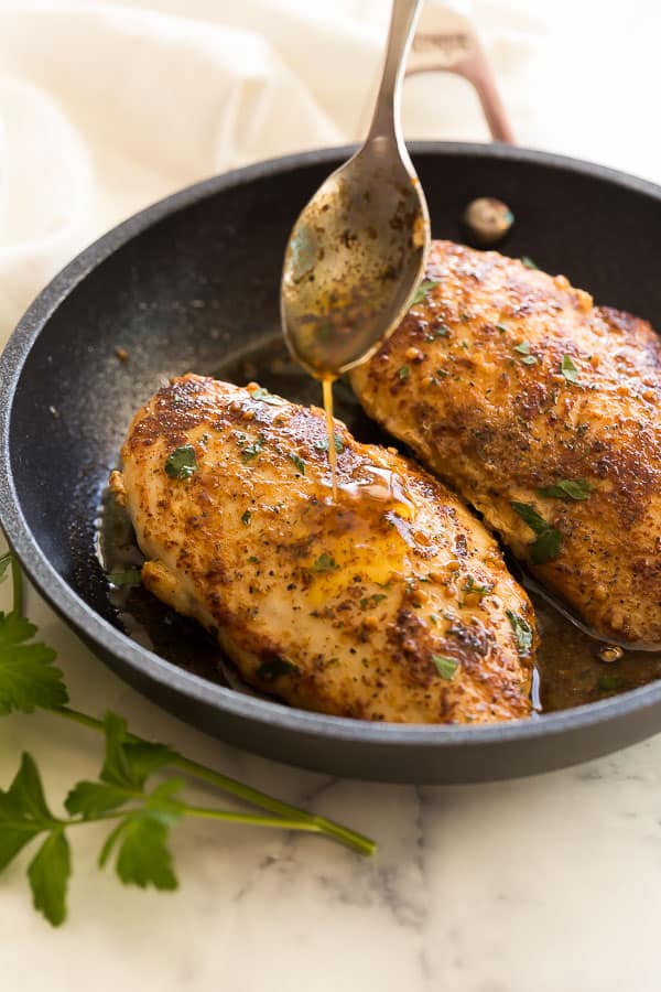 These easy Pan Fried Chicken Breasts come together quickly in one skillet! An easy garlic butter sauce makes these a family favorite. #chicken #chickenbreasts #dinner #healthyrecipe chicken breasts being drizzled with garlic butter sauce in pan