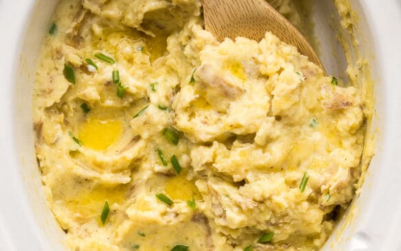 overhead image of slow cooker mashed potatoes with wooden spoon