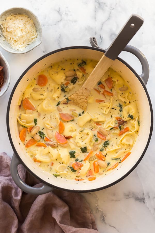 This Creamy Spinach Tortellini Soup is filled with white beans and Grana Padano, topped with crispy Prosciutto di Parma! It is a comforting and flavorful easy dinner idea! #soup #tortellini #dinner #recipes overhead image of spinach tortellini soup in grey dutch oven