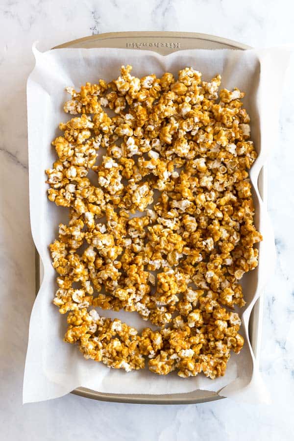 This Caramel Popcorn is an easy, sweet and salty treat that everyone loves! Crispy and crunchy without being hard, no candy thermometer required! #popcorn #caramel #christmas #recipes overhead image of caramel popcorn on parchment lined baking sheet