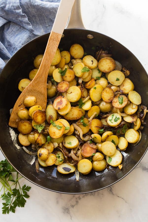 Lyonnaise Potatoes are thinly sliced potatoes, par boiled and fried until crispy with caramelized onions -- simple ingredients and big flavor! #potatoes #sides #recipes #skillet overhead image of lyonnaise potatoes in black skillet