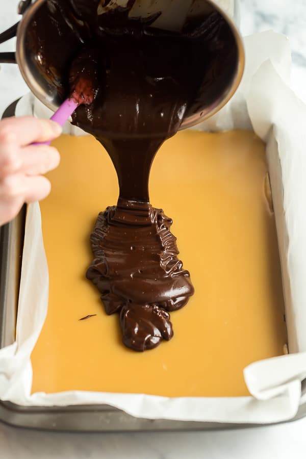 chocolate ganache being poured on caramel in pan