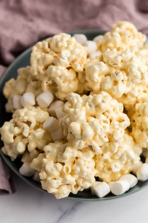 These Popcorn Balls are a fun holiday treat that the kids love! Experiment with flavors and colors to create something special for any occasion. #popcorn #christmas #holidays #recipes stack of popcorn balls in blue bowl
