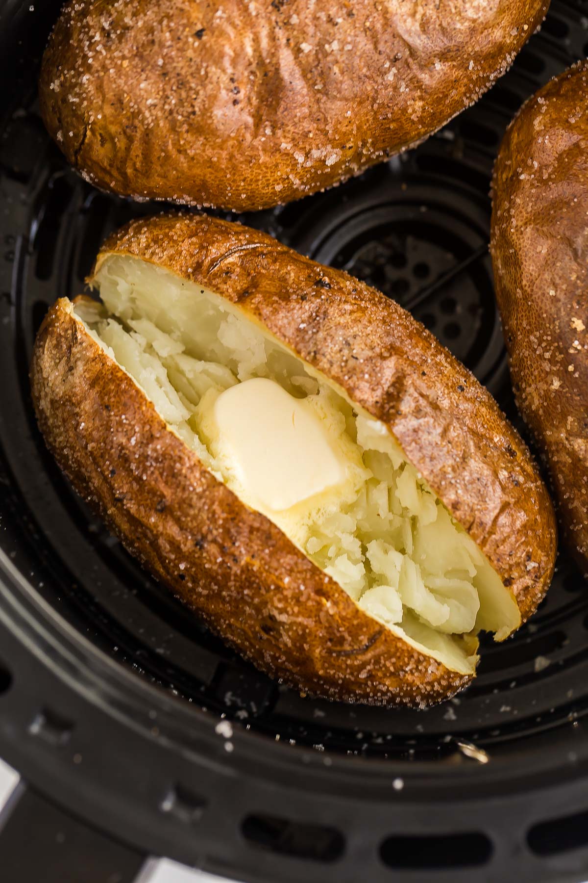 baked potato in air fryer basket cut open with butter.