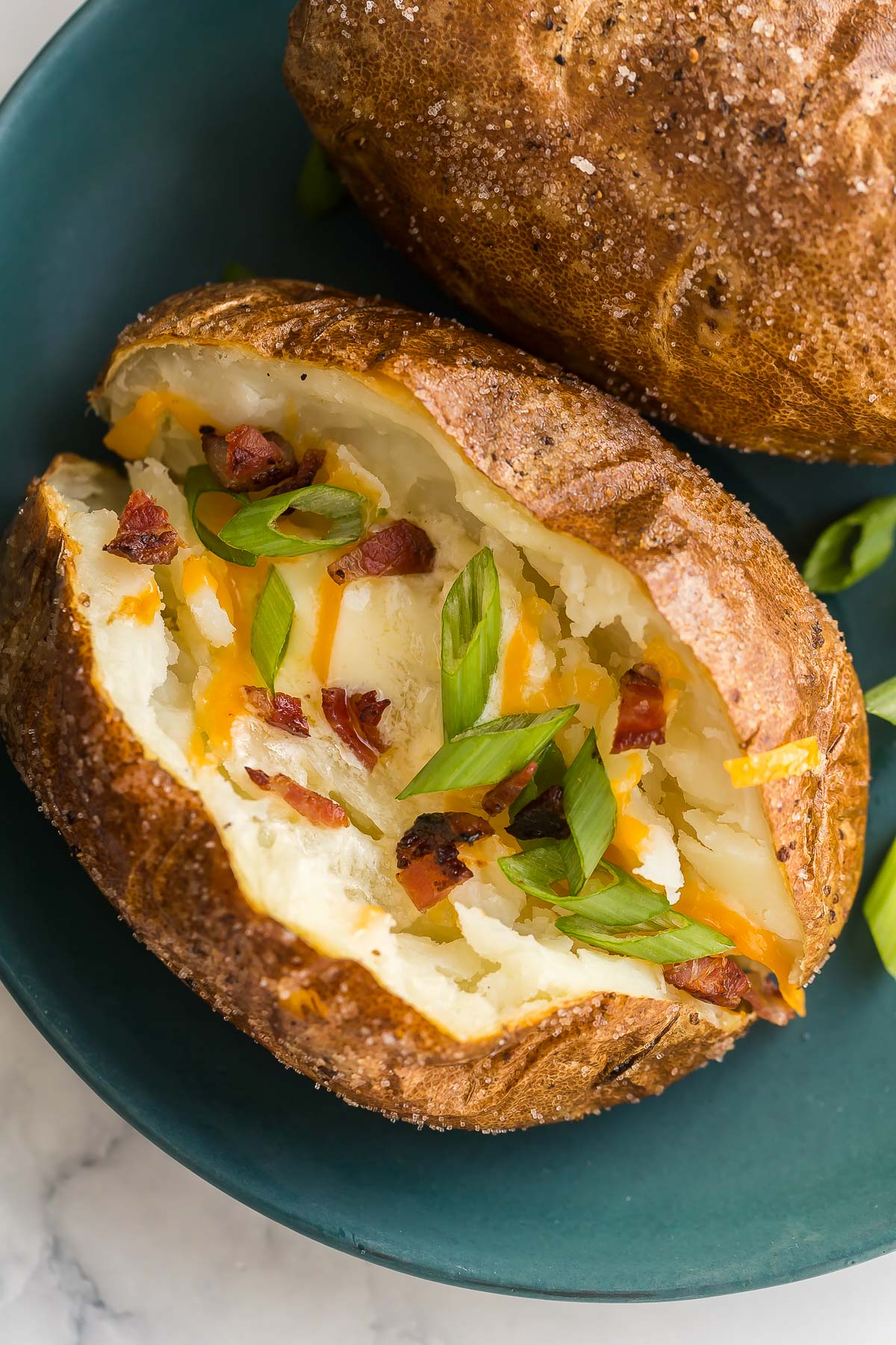 close up image of air fryer baked potato with cheese green onions and bacon.