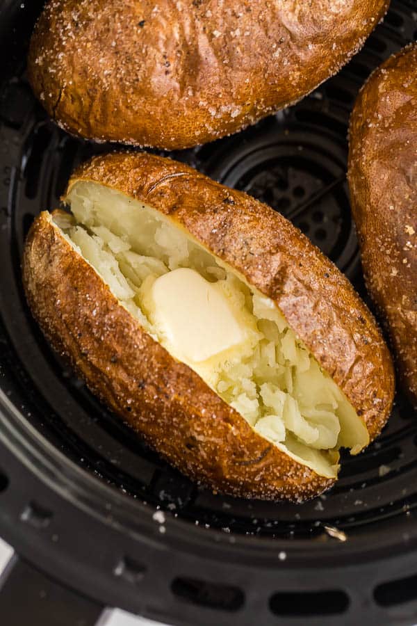 air fryer baked potato in basket cur open with butter