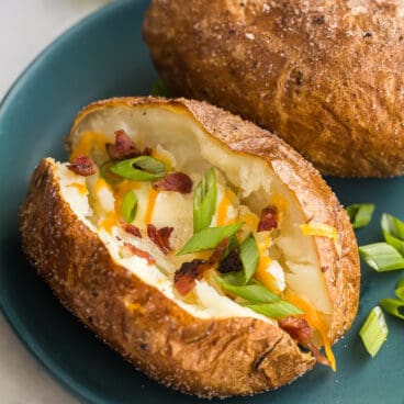 baked potato on plate cut open with green onions cheese and bacon