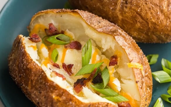 baked potato on plate cut open with green onions cheese and bacon