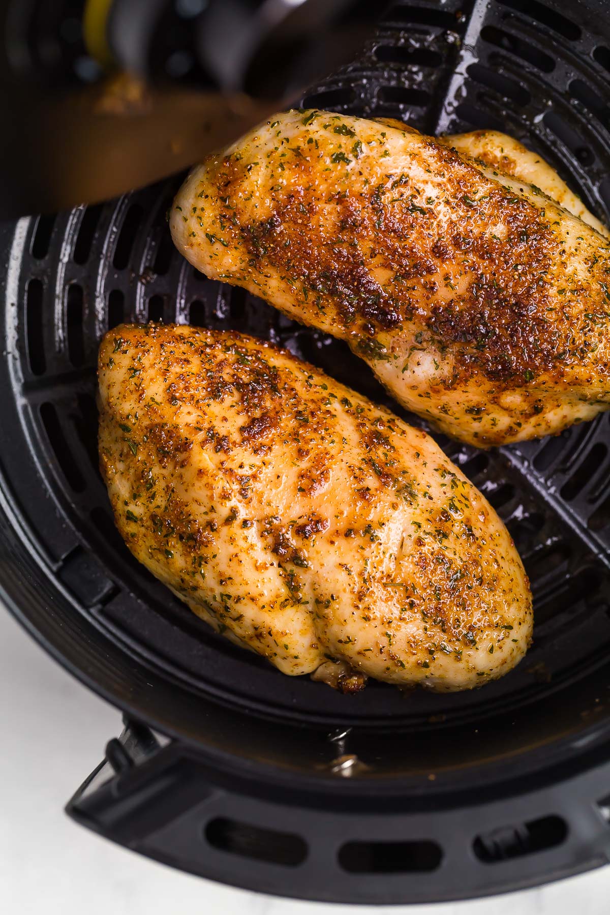 overhead image of two air fryer chicken breasts in air fryer basket.