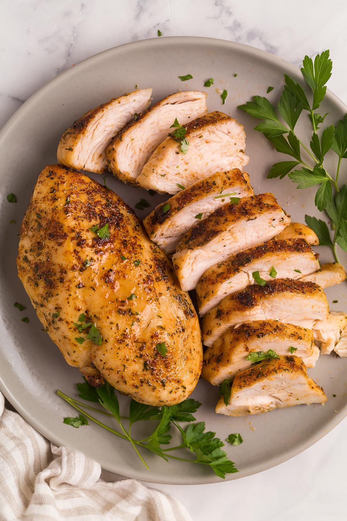 plate with one whole chicken breast and one sliced chicken breast.