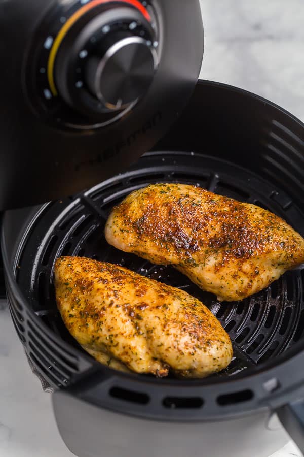 basket being pulled out of air fryer with chicken breast inside