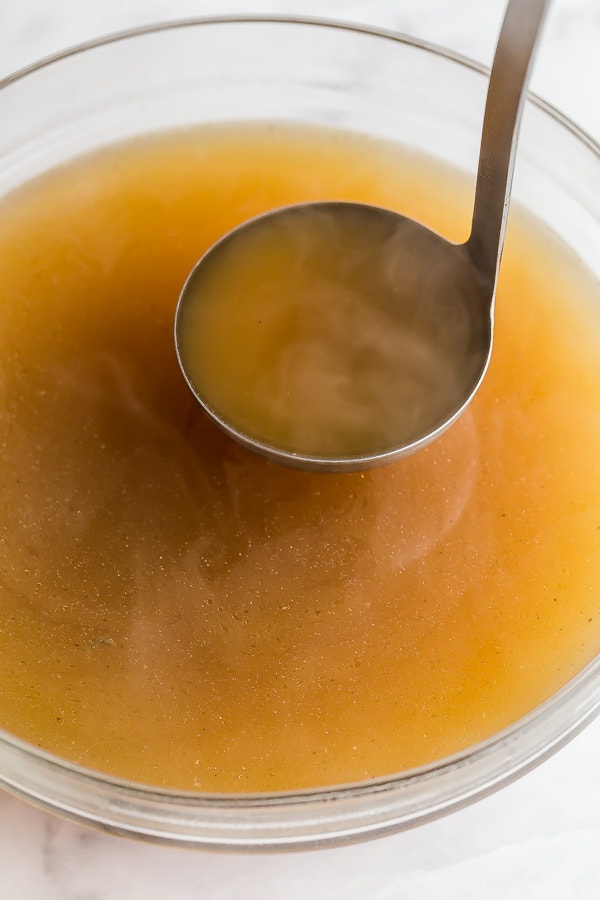 close up image of ladle scooping chicken broth from bowl