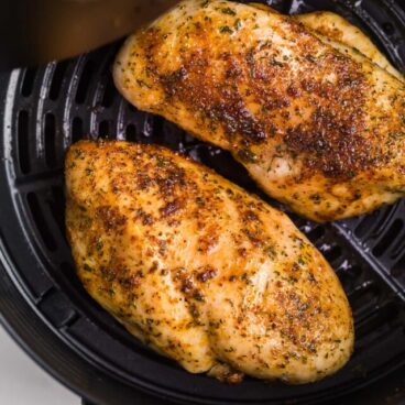 overhead image of two air fryer chicken breasts in air fryer basket.