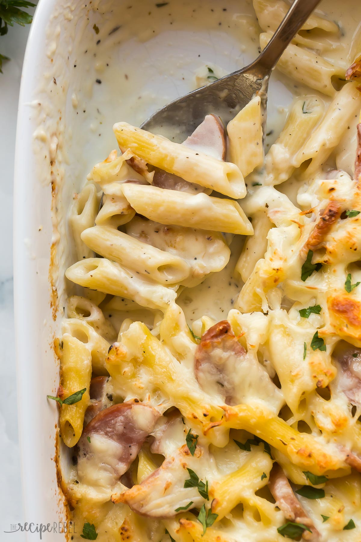 close up image of metal spoon scooping bake penne pasta with kielbasa