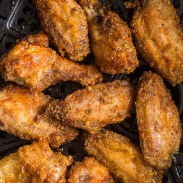 close up image of cooked chicken wings in air fryer basket with no sauce