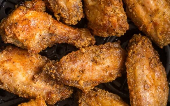 close up image of cooked chicken wings in air fryer basket with no sauce