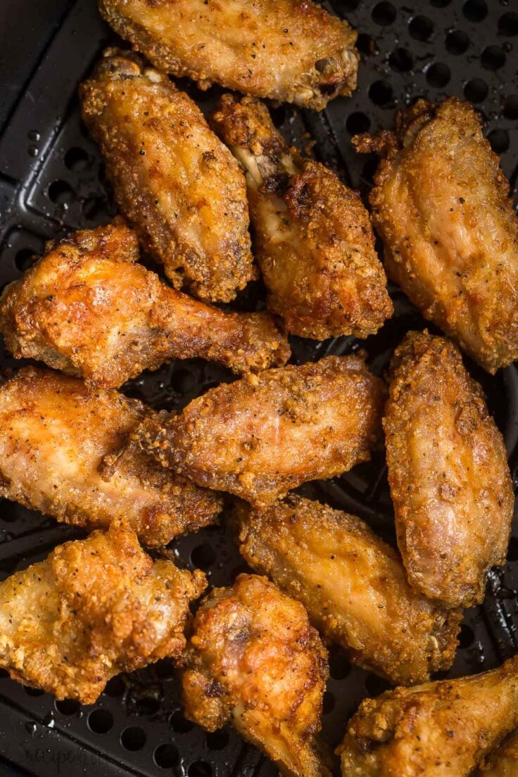 close up image of cooked chicken wings in air fryer basket with no sauce