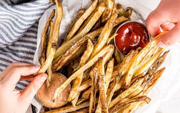 overhead image of hands grabbing air fryer french fries