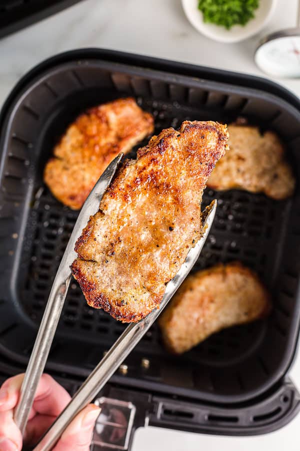 These air fryer pork chops make a fast and flavorful week night meal. Simple seasoning, easy prep and so juicy! #airfryer #recipes #pork #porkchops tongs holding air fryer pork chop over basket