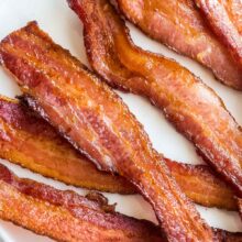close up image of crispy air fryer bacon on white plate on white background