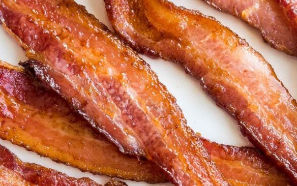 close up image of crispy air fryer bacon on white plate on white background