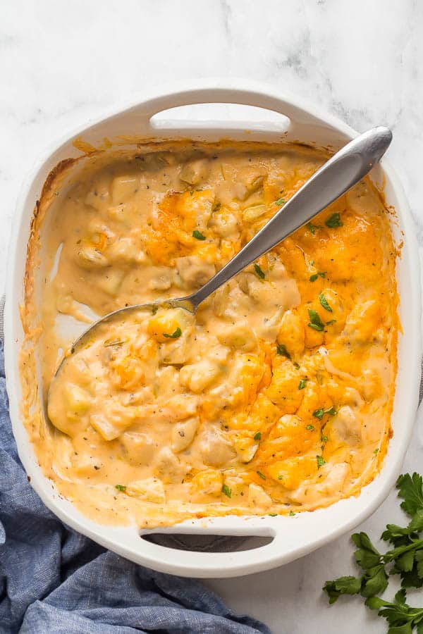 overhead image of cheesy potatoes in white casserole dish with spoon