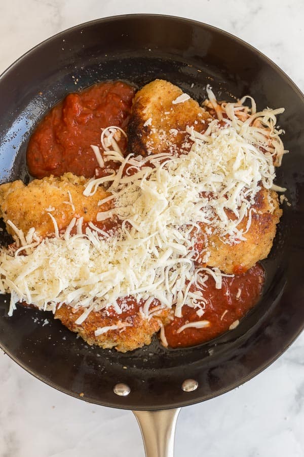 browned chicken breasts in pan with sauce and cheese