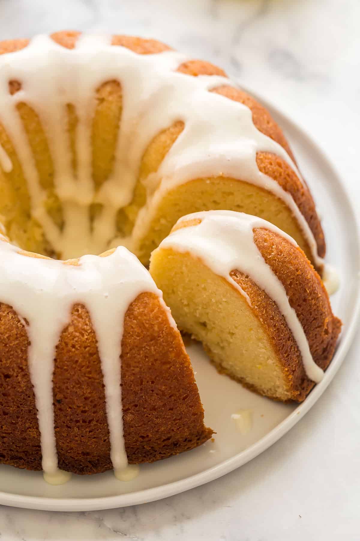 This Lemon Bundt Cake is so moist and packed with lemon flavor! It's full of real lemon flavor, topped with a lemon cream cheese glaze and berries. #lemon #cake #recipe | dessert recipes | lemon recipes | easy cake recipes | easter cake recipes | greek yogurt cake | easter treats | easter cake | spring desserts | bundt cakes close up image of a lemon bundt cake with one piece cut.