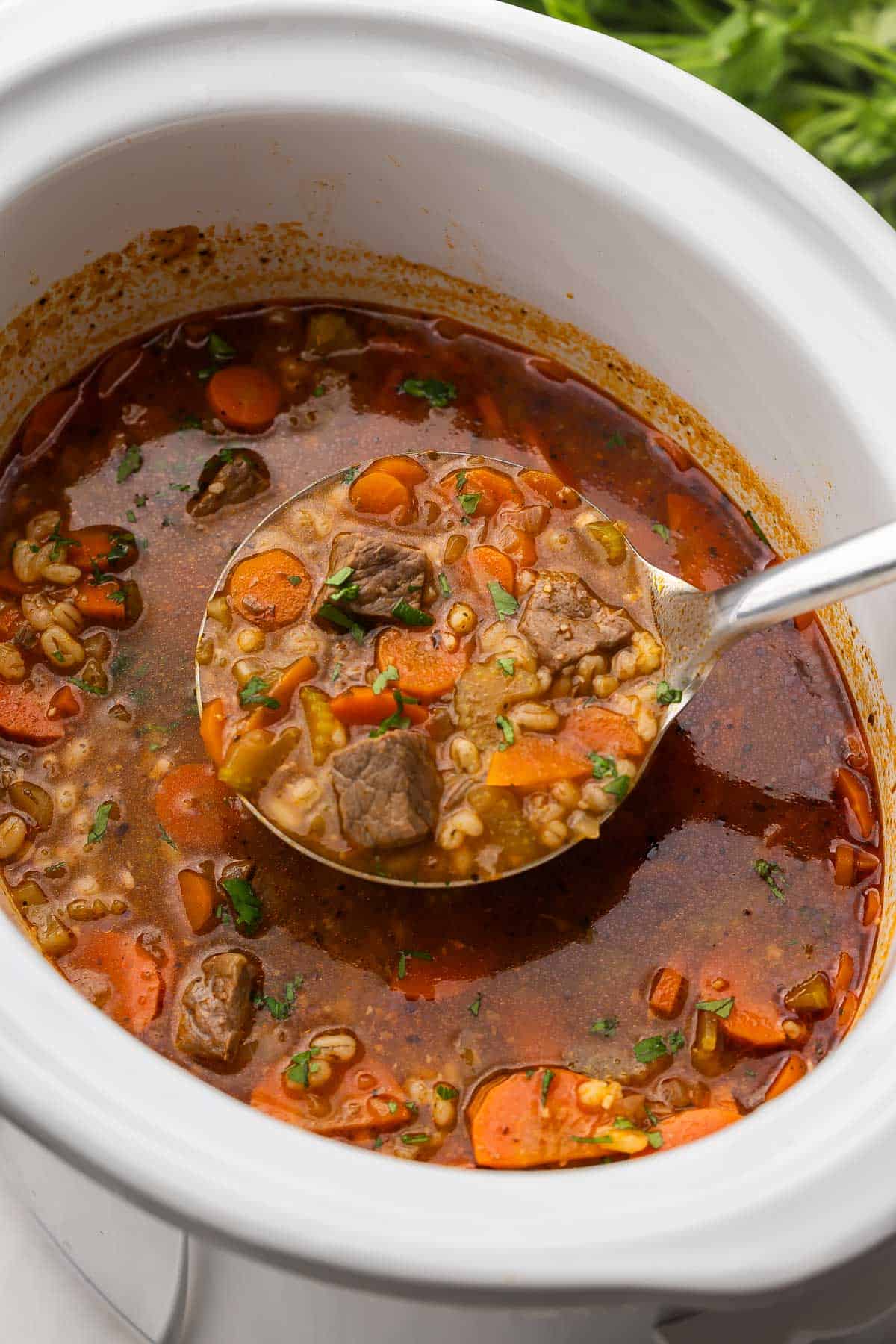 close up image of a metal ladle scooping slow cooker beef barley soup.