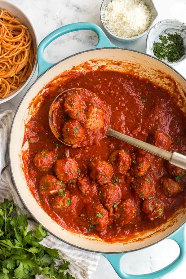 overhead image of meatballs in tomato sauce with metal ladle