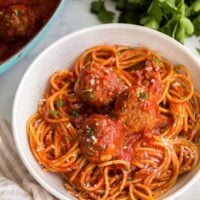 close up of spaghetti and meatballs in white bowl