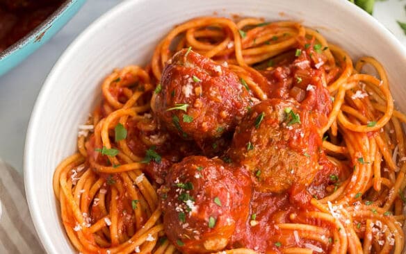 close up of spaghetti and meatballs in white bowl