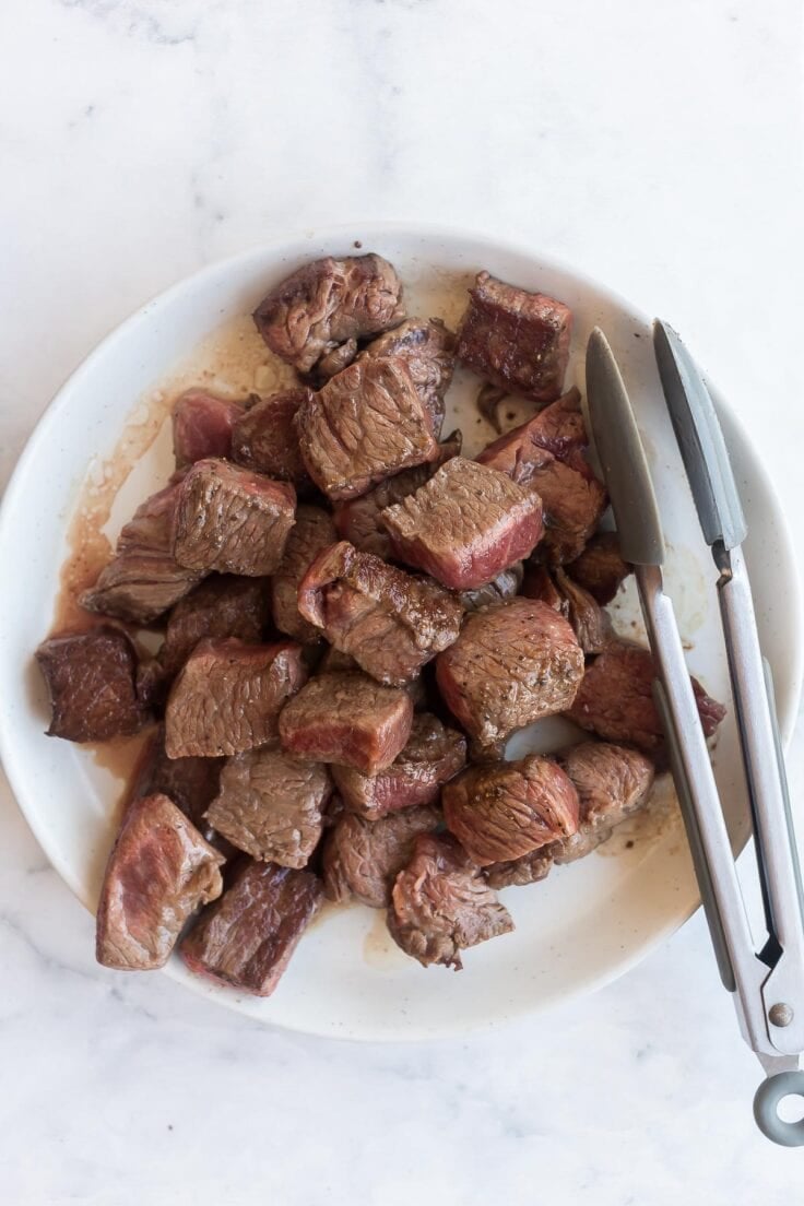 browned beef chunks on a plate with tongs.