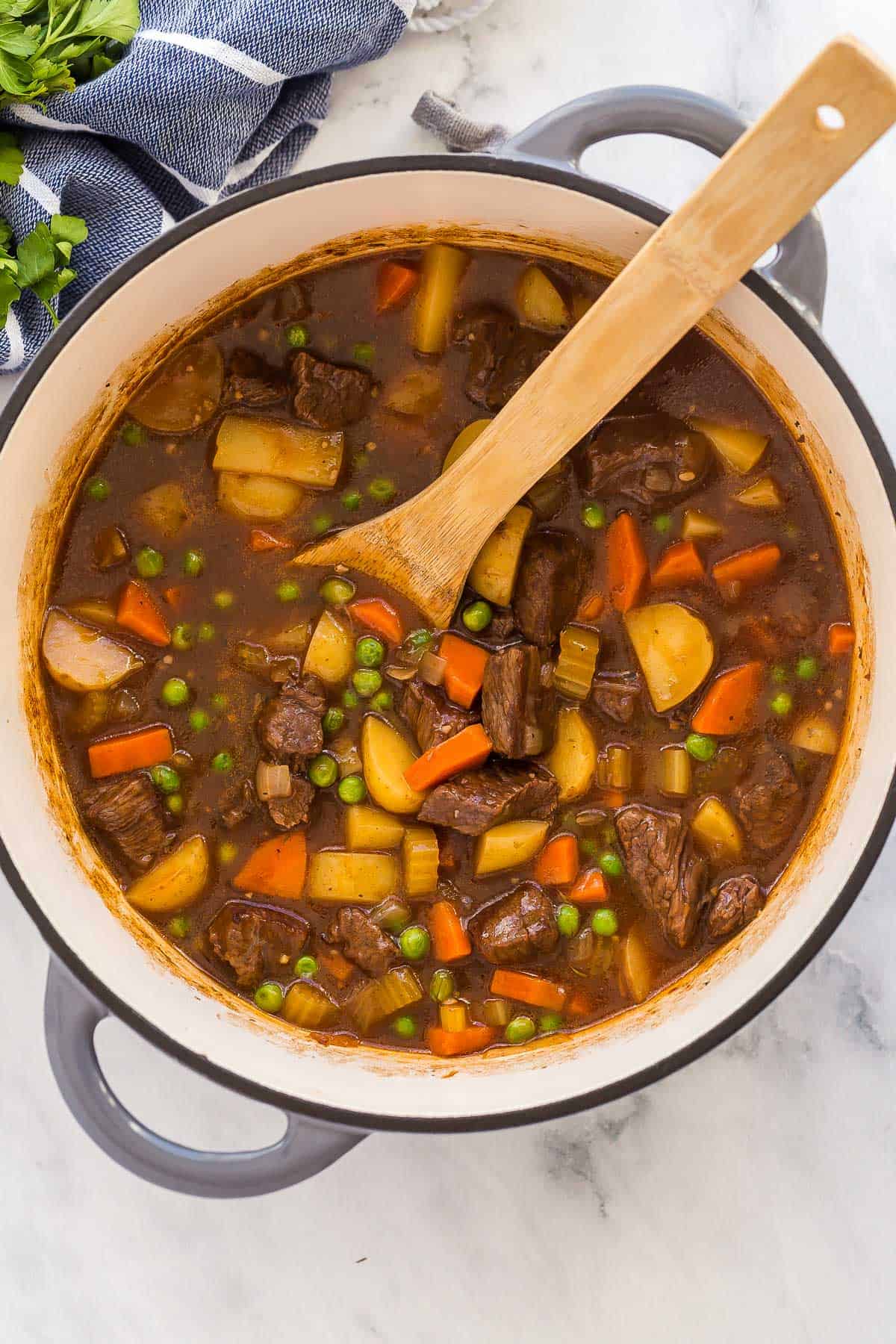 overhead image of beef stew in pot with wooden spoon.